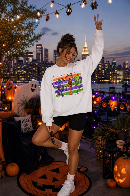 Dancing pumpkin head skeleton trio Halloween crewneck sweatshirt in purple orange and green on white worn by a model
