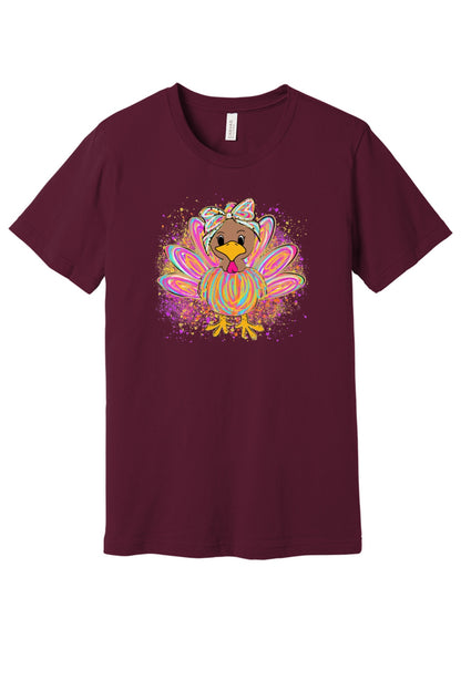 Colorful cartoon girl turkey with bow and tie-dye swirl feathers printed on a unisex Thanksgiving tee in Maroon