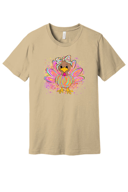 Colorful cartoon girl turkey with bow and tie-dye swirl feathers printed on a unisex Thanksgiving tee in Soft Cream