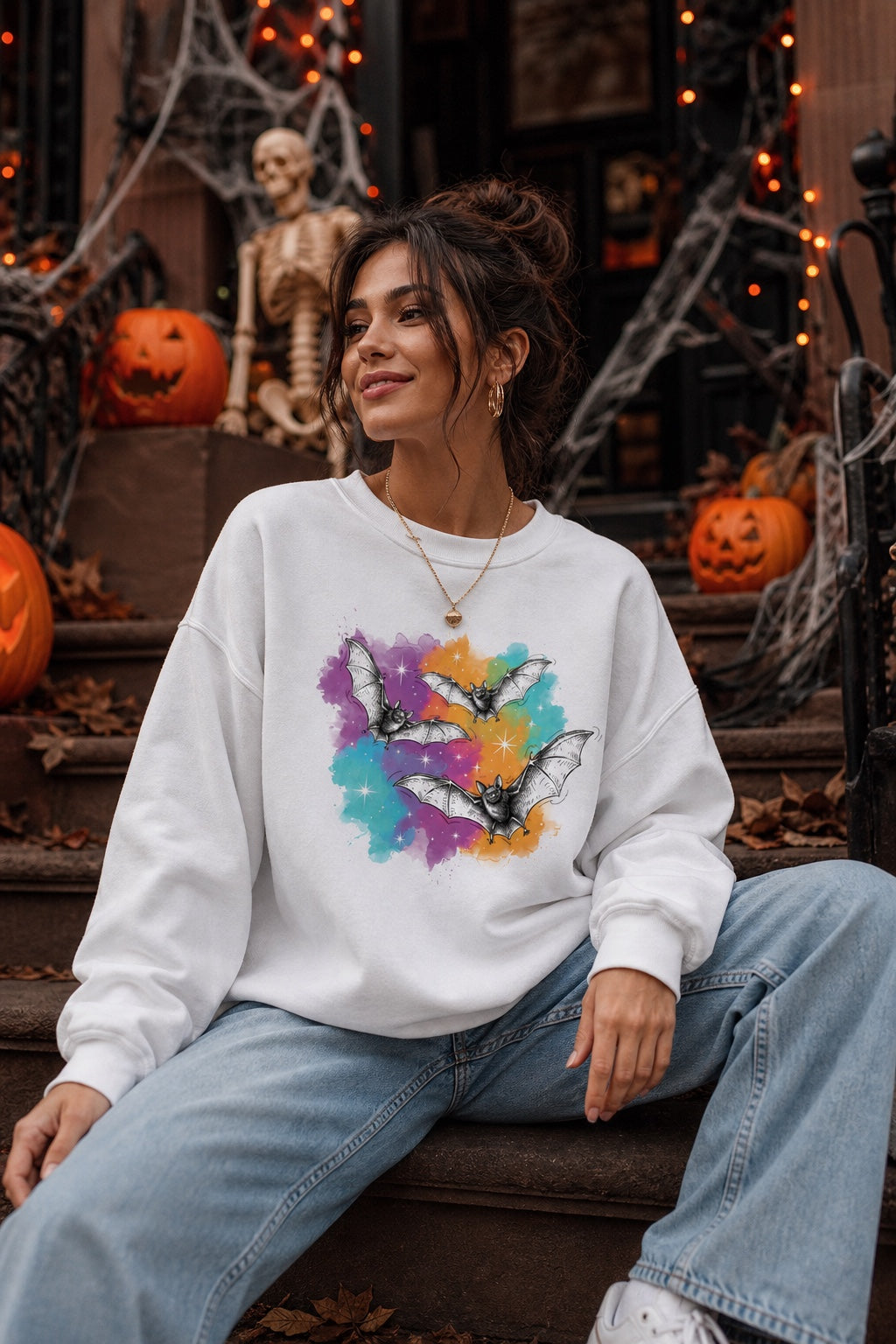 Gildan 18000 crewneck sweatshirt with three sketch-style flying bats over a watercolor purple teal orange sparkle Halloween print worn by a model