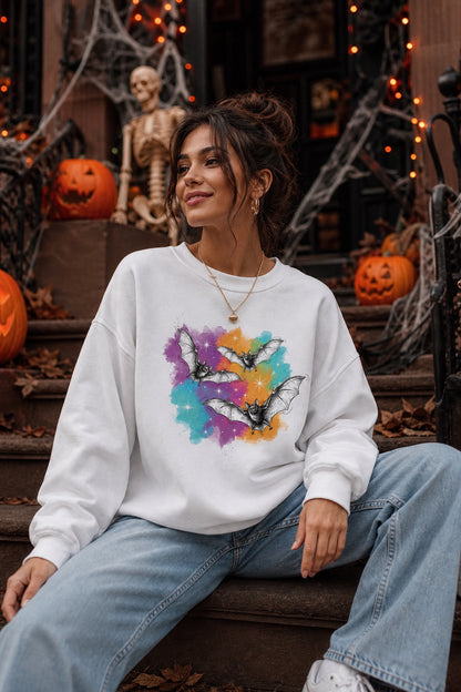 Gildan 18000 crewneck sweatshirt with three sketch-style flying bats over a watercolor purple teal orange sparkle Halloween print worn by a model
